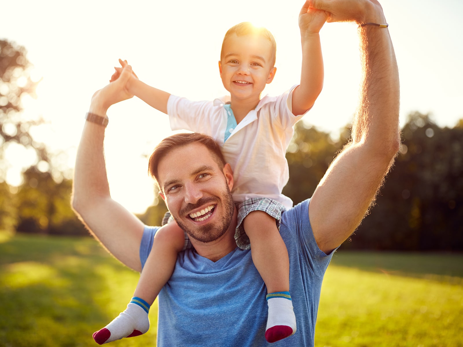 Man with child on shoulder hands up to the sky