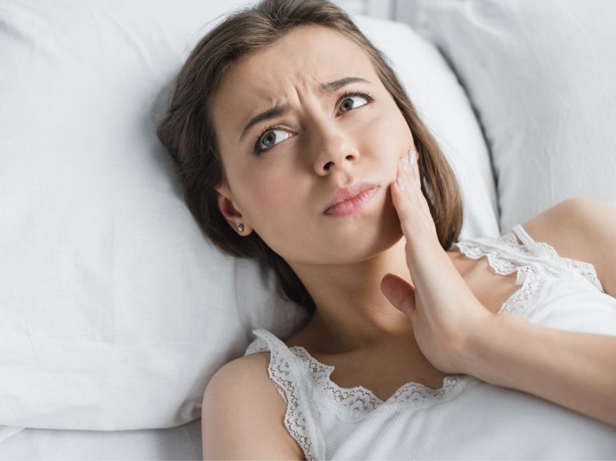 woman laying in bed grabbing jaw in pain