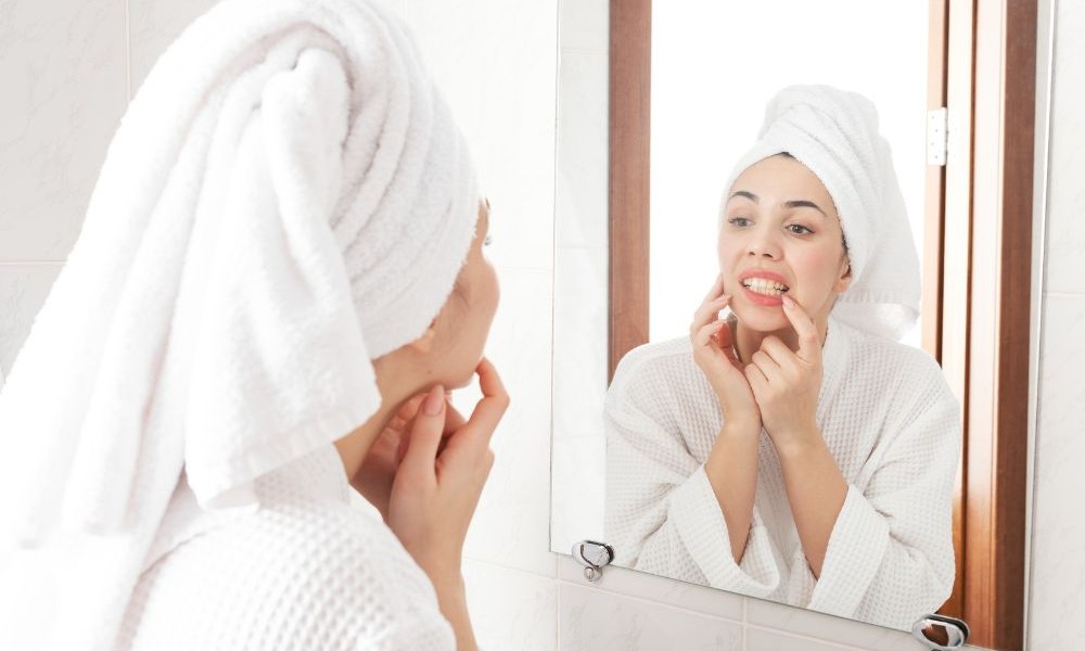 woman with towel around hair looking at teeth in mirror