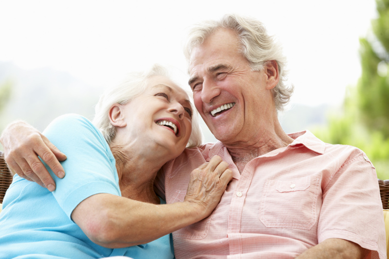 A happy older couple with dentures enjoy a laugh and a smile together while sitting outside