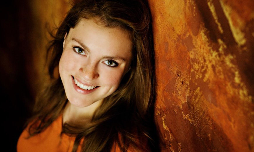 A young woman leans against a wall, showing off her amazing dental crowns thanks to Dr. Skinner